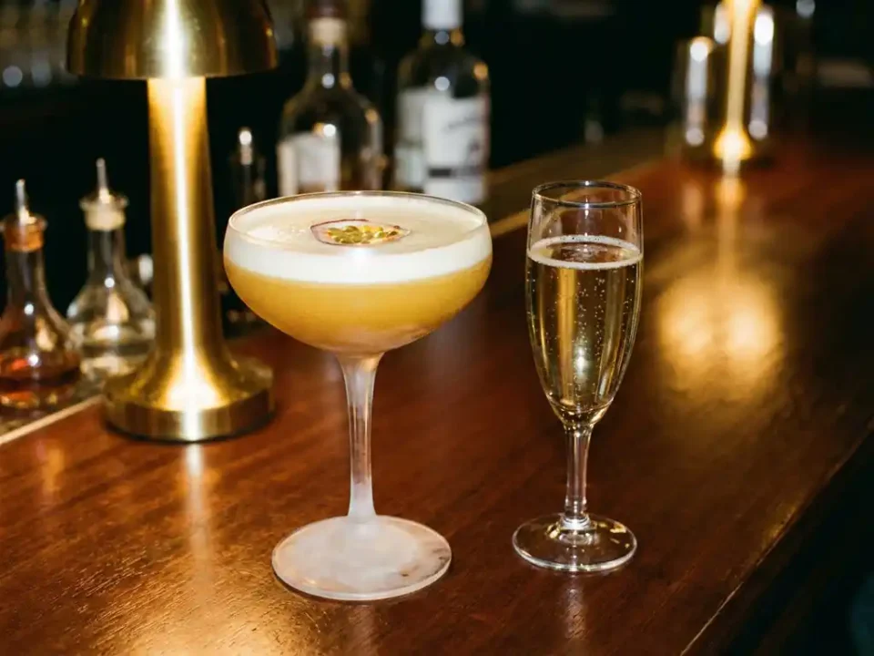Pornstar Martini Cocktail im eleganten Coupe-Glas mit Passionsfrucht und Champagner-Shot auf Mahagoni-Bar